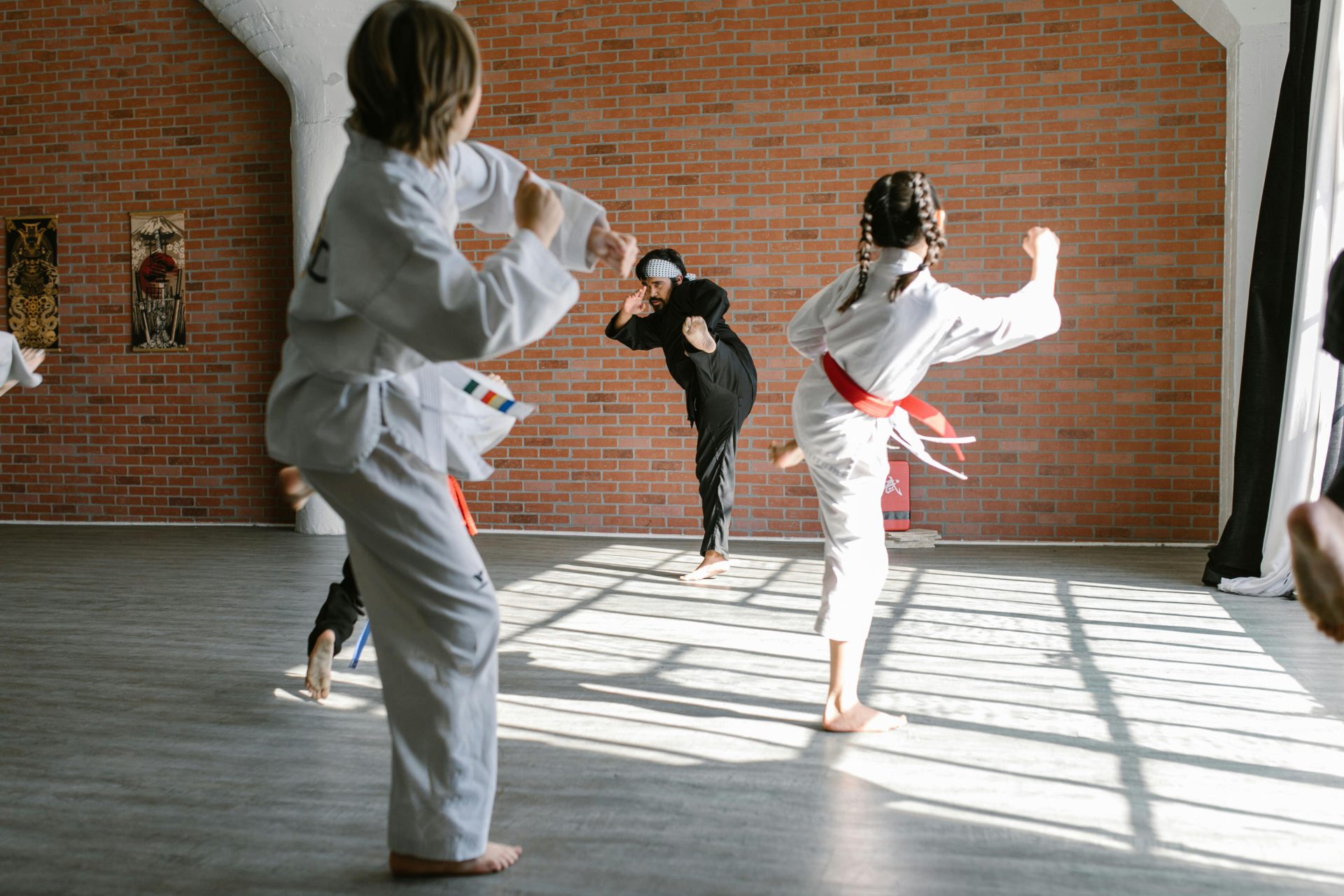 Grupo de niños practicando patadas de karate en un dojo con un instructor.